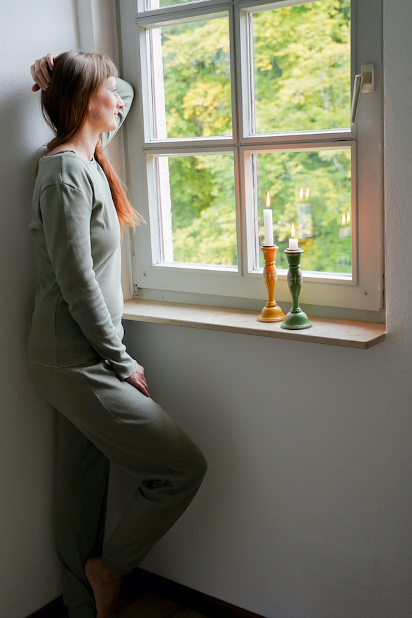 Eine Frau steht vor dem Fenster. neben ihr zwei Kerzen. Sie schaut aus dem Fenster und trägt einen selbstgenähten Schlafanzug nach Schnittmuster