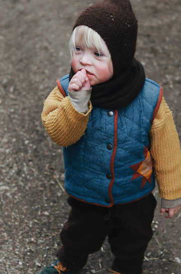 Ein Junge mit Downsyndrom steht auf einem Weg. Er trägt die gequiltete Weste Malus.