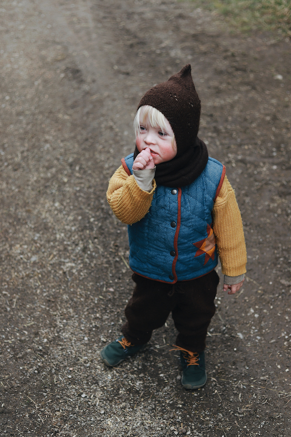 Ein Junge mit Downsyndrom steht auf einem Weg. Er trägt die gequiltete Weste Malus.