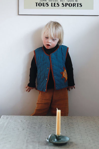 Ein Kind steht vor einer Kerze und trägt die genähte Veste Malus